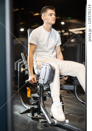 In gym, guy uses gym apparatus to strengthen leg muscles 126576114