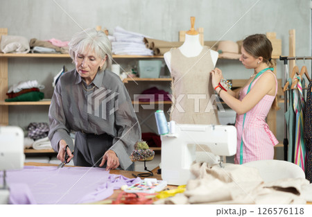 Mature female dressmaker cutting textile other work with mannequin Mature female dressmaker cutting textile other work with mannequin 126576118
