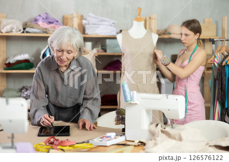 Mature female dressmaker drawing in tablet other work with mannequin Mature female dressmaker drawing in tablet other work with mannequin 126576122