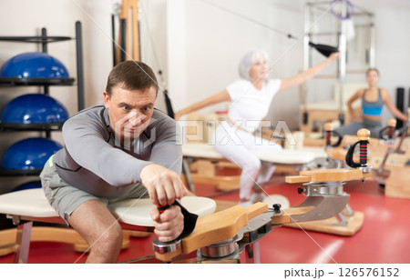Man during Pilates training performs exercises and tasks on heron pulley tower Man during Pilates training performs exercises and tasks on heron pulley tower 126576152