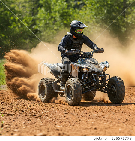 A person wearing protective gear rides an all-terrain vehicle, kicking up a large cloud of dirt and dust on an off-road course 126576775