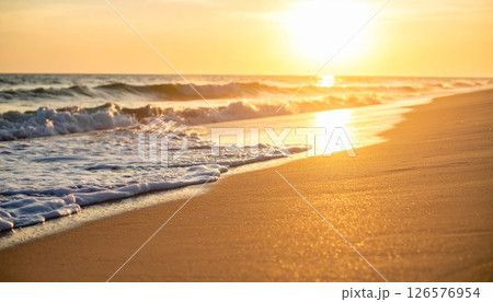 Warm sunlight paints the desert landscape and mountain horizons, with the sun setting over calm ocean waves or rising above sandy beaches under a beautiful sky 126576954