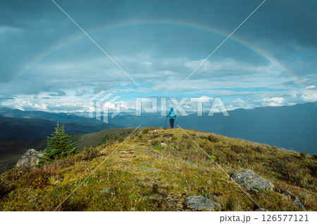 Woman backpacker hiking on high altitude mountain top after the rain,face a beautiful rainbow 126577121