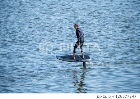 Man on an eFoil board gliding over calm blue water Man on an eFoil board gliding over calm blue water 126577247