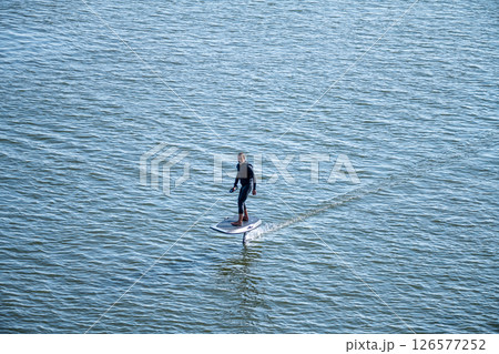 Man on an eFoil board gliding over calm blue water 126577252