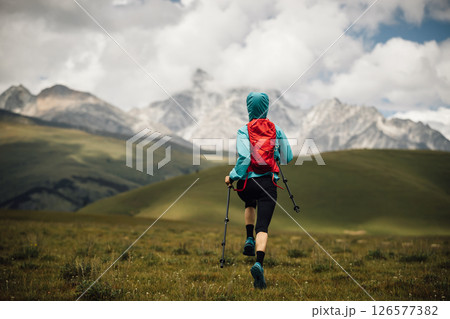 Fitness woman trail runner running in grassland with snow capped mountains in the background 126577382