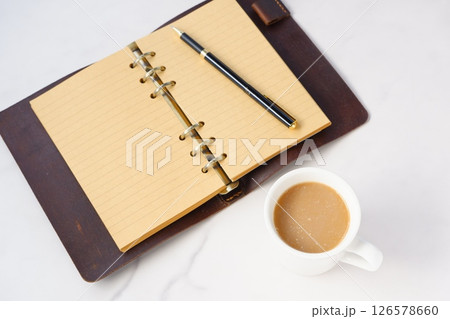 ミルクをたっぷり入れたコーヒー、カフェ・ラッテを飲みながら、システム手帳でデスクワーク中のイメージ 126578660
