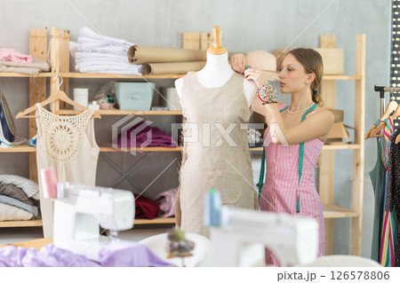 Designer in dress standing near mannequin in workshop Designer in dress standing near mannequin in workshop 126578806