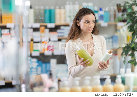 In drug store, woman examine antidandruff shampoo 126578827