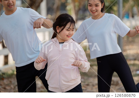 Family having fun exercising together, daughter dancing joyfully while parents join her in playful movement Family having fun exercising together, daughter dancing joyfully while parents join her in playful movement 126580870