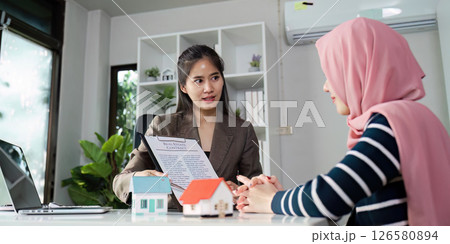 Real estate agent explaining a contract to a client with model houses on the table. Real estate agent explaining a contract to a client with model houses on the table. 126580894