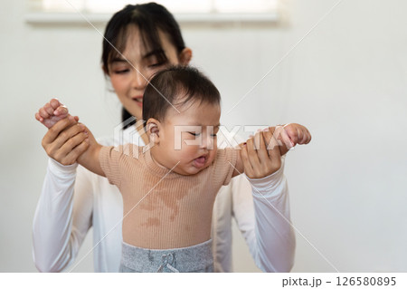 Parenting and early development. Mother helping her baby practice standing and balancing for physical growth. Parenting and early development. Mother helping her baby practice standing and balancing for physical growth. 126580895