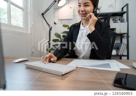 Professional Asian female call center agent assisting clients with inquiries in a modern workspace, showcasing effective communication. 126580903