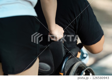 Inclusive Support and Mobility: Close-Up of a Caregiver Assisting a Person in a Wheelchair Outdoors 126580943