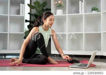 Young woman engaging in a virtual workout session on a laptop, promoting wellness. Young woman engaging in a virtual workout session on a laptop, promoting wellness. 126580952