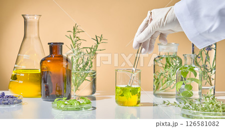 Scientist pouring vibrant yellow herbal extract into a beaker, surrounded by glassware, fresh greens, and lavender on lab table. Glass chopsticks in hand to stir the golden oil of herbs Scientist pouring vibrant yellow herbal extract into a beaker, surrounded by glassware, fresh greens, and lavender on lab table. Glass chopsticks in hand to stir the golden oil of herbs 126581082