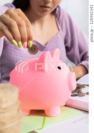 A Young Woman Diligently Saving Coins in a Pink Piggy Bank for Future Financial Goals A Young Woman Diligently Saving Coins in a Pink Piggy Bank for Future Financial Goals 126581341