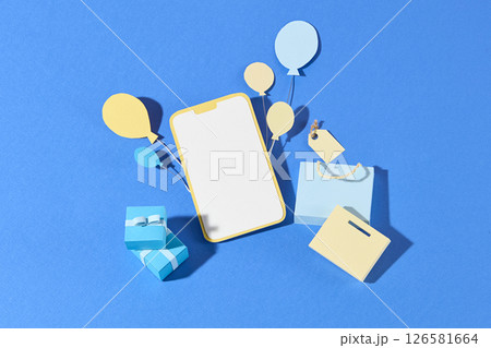 A smart phone lies in the center with gift boxes and paper icons scattered around on a dual blue background, portraying e-shopping and discounts. Flat lay, empty space for 126581664