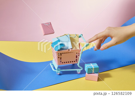 Girl gently pushing a shopping cart filled with colorful shopping bags and boxes. Eye-catching colors of blue, yellow and pink. Conveys convenient shopping, advertising image, design space 126582109