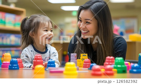 Joyful toddler and smiling teacher play with colorful stacking c 126582392