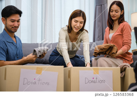 group of friend  sorting and packing clothes into a donation box.community support, and charitable giving 126583368