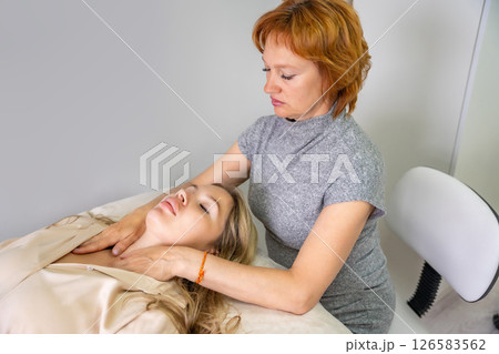 Female practitioner performs facial lifting technique on a young woman lying on a couch. Concept of energy healing, face therapy and alternative wellness practice from Access Bars. 126583562