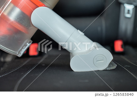 Handheld cordless vacuum cleaner vacuuming car seat upholstery. Modern car interior cleaning and maintenance Handheld cordless vacuum cleaner vacuuming car seat upholstery. Modern car interior cleaning and maintenance 126583840