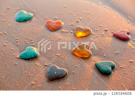 Heart shaped sea pebbles in vibrant colors like turquoise, coral, amber and jade naturally arranged on wet beach sand 126584608