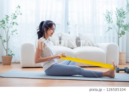 Young Asian woman doing pilates workout using elastic strap pulling with arms 126585104