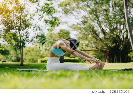 Young Asian woman doing yoga stretching on green grass 126585105