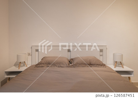 Front view of bedroom with taupe bedding, white bedframe and matching nightstands and lamps Front view of bedroom with taupe bedding, white bedframe and matching nightstands and lamps 126587451