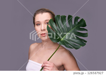 Young caucasian female with monstera leaf posing against neutral background Young caucasian female with monstera leaf posing against neutral background 126587927