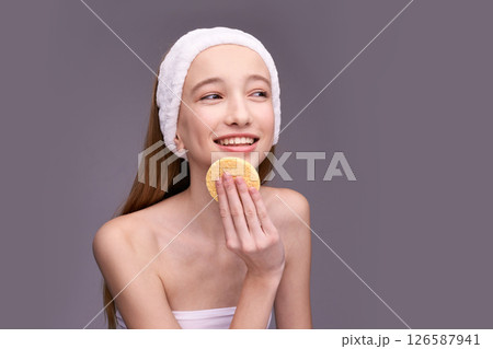 Smiling caucasian female teen using facial sponge for skin care routine 126587941