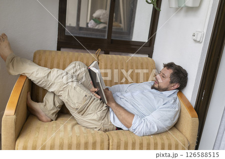 Man relaxing on sofa reading a book on balcony Man relaxing on sofa reading a book on balcony 126588515