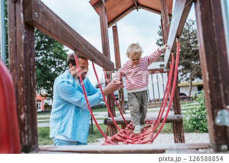 Toddler crossing playground obstacle with dad's support Toddler crossing playground obstacle with dad's support 126588854