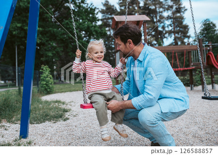 Father swinging small son on playground swing. 126588857