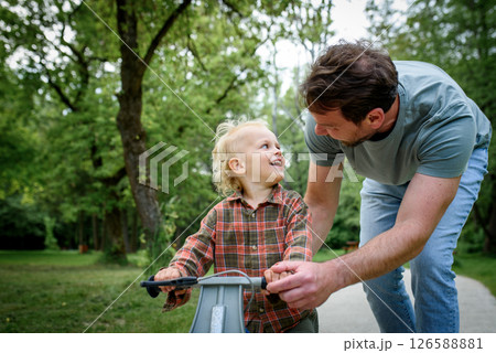 Proud dad watching son ride his balance bike in the park. 126588881