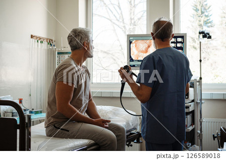 Doctor explaining colonoscopy results to patient using monitor images. 126589018