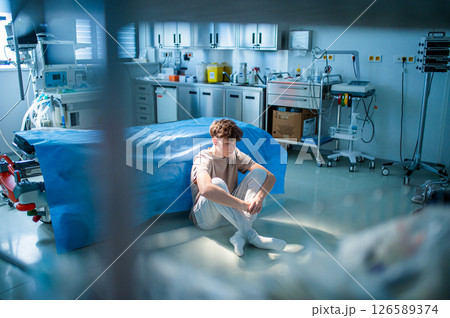Teenage boy sitting depressed on hospital floor, struggling with mental health issues. 126589374