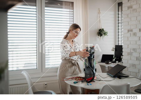 Female engineer building and programming a robotic arm at home. 126589505