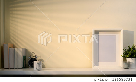 Minimalist workspace with empty frame, plants, books, and accessories in soft morning light 126589731