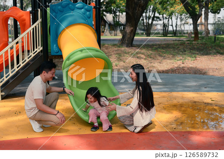 Smiling parents and two young children enjoy playtime at a colorful playground Smiling parents and two young children enjoy playtime at a colorful playground 126589732