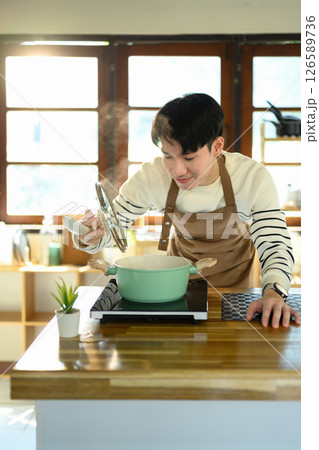 Happy Asian man preparing a meal on a modern stovetop 126589736
