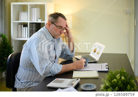 Serious senior man checking business reports and analyzing charts on laptop Serious senior man checking business reports and analyzing charts on laptop 126589759