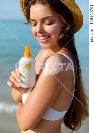 Beautiful Woman in Bikini Applying Sun Cream on Tanned Shoulder. Sun Protection. Skin and Body Care. Girl Using Sunscreen. Portrait Of Female Holding Suntan Lotion or Moisturizing Sunblock. Beautiful Woman in Bikini Applying Sun Cream on Tanned Shoulder. Sun Protection. Skin and Body Care. Girl Using Sunscreen. Portrait Of Female Holding Suntan Lotion or Moisturizing Sunblock. 126590701