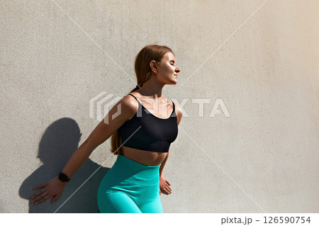 Fitness enthusiast stretching against a concrete wall in stylish activewear showcasing strength and determination, healthy lifestyle concept 126590754
