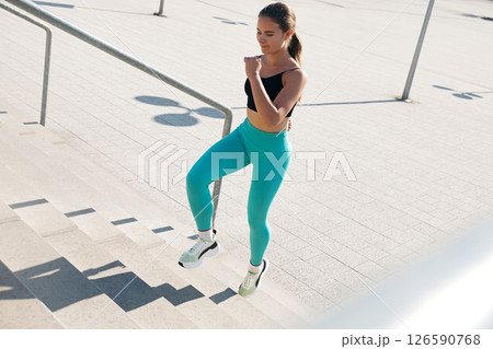 A young athletic woman with a fit body is seen confidently ascending outdoor stairs. Girl wears fitted workout clothes, demonstrating her commitment to a healthy lifestyle. 126590768