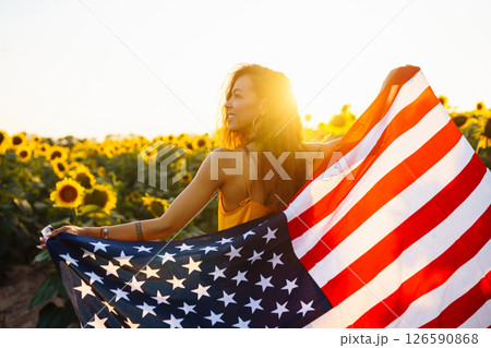 Woman proudly hold waving american USA flag in in the sunflower field. Independence Day, 4th July. 126590868
