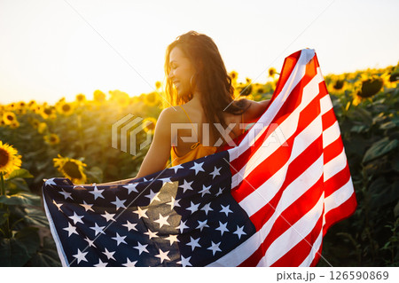 Woman proudly hold waving american USA flag in in the sunflower field. Independence Day, 4th July. Woman proudly hold waving american USA flag in in the sunflower field. Independence Day, 4th July. 126590869