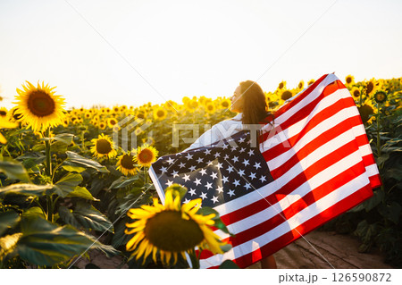 Woman proudly hold waving american USA flag in in the sunflower field. Independence Day, 4th July. 126590872